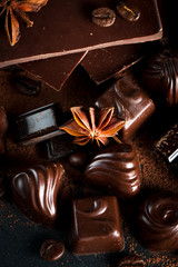 Assortment of dark, white and milk chocolate stack, chips. Chocolate and coffee beans on rustic wooden sacking background. Spices, cinnamon. Selective macro focus. Chocolates background. Sweets