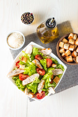 Fresh salad made of tomato, ruccola, chicken breast, eggs, arugula, crackers and spices. Caesar salad in a white, transparent bowl on wooden background