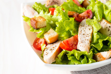 Fresh salad made of tomato, ruccola, chicken breast, eggs, arugula, crackers and spices. Caesar salad in a white, transparent bowl on wooden background