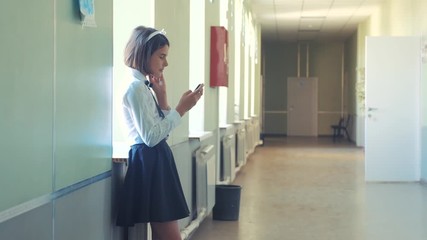 schoolgirl education with smartphones at school concept lifestyle . Young girl teen and using smartphone standing by the window in the corridor of the school. correspondent in the messenger, write a - Powered by Adobe