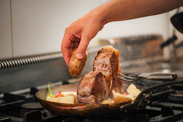 Preparing delicious food, t-bone steak, potatoes and vegetables on pan.