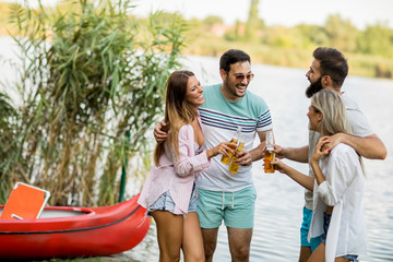 Group of friends with cider bottles standing by the boat near the beautiful lake and having fun