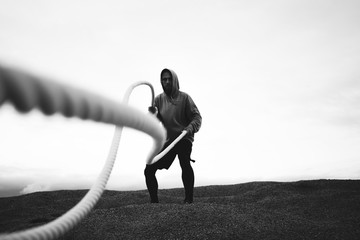 Brave athlete wearing sportswear doing intens workout using battle ropes on outdoor. Fitness brave...