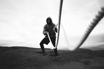 Brave athlete wearing sportswear doing intens workout using battle ropes on outdoor. Fitness brave...