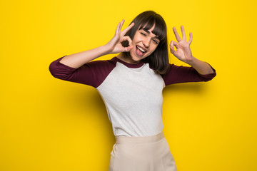 Fototapeta premium Portrait of a cheerful happy pleased young pretty woman showing okay gesture posing isolated over yellow wall background.
