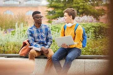 Portrait of two international students chatting while relaxing outdoors in college campus, copy...