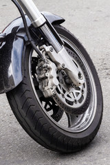 Close-up of the front wheel of a motorcycle and brake disc. Chrome fork and black motorbike wing