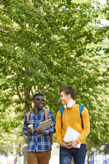 Portrait of two international college students chatting cheerfully while walking to school, copy space