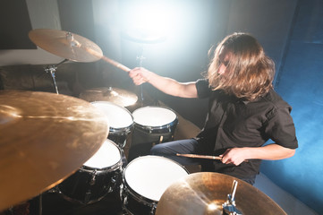 Fototapeta na wymiar Portrait of a long-haired drummer with chopsticks in his hands sitting behind a drum set. Low key. Concepts of the creative freedom of the millenial generation