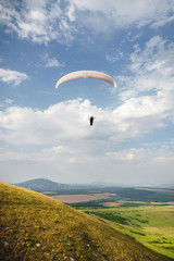 A paraglider flies in the sky in a cocoon suit on a paraglider over the Caucasian countryside with hills and mountains. Paragliding Sport Concept