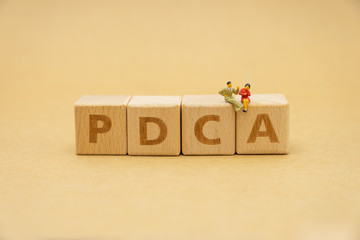 Miniature people sitting on wood word PDCA using as background business concept and Strategy concept with copy space for your text or design.