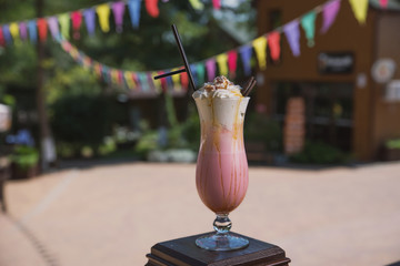 Cocktail with strawberry ice cream, caramel, cream and chocolate cookies on the background of spring greens and colored flags