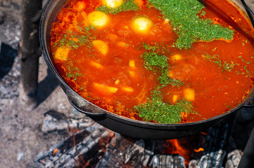 Ukrainian borsch. Traditional red soup in a large metal cauldron on a bonfire. Cooking on a camping trip.