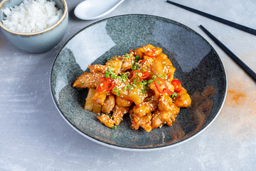 Bowl with sweet and sour chicken, rice, apple, peanuts, hot chili. Flat lay pan-asian food. Traditional Chinese lunch. Healthy, restaurant food concept on grey stone background.