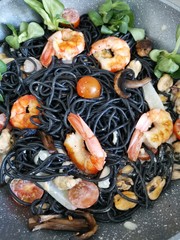 Fresh black tagliolini pasta with  seafood in herbs on corn salad and tomatoes.