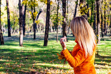 Autumn girl in an orange sweater straightens her blond hair.