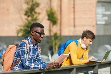 Portrait of African-American student reading book outdoors in sunlight, copy space