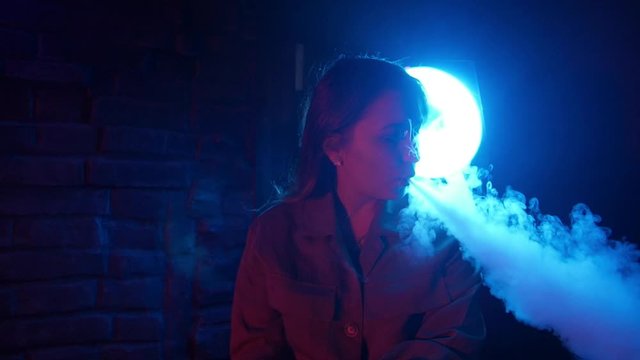 Young woman in neon red and blue smoke with vape or e-cigarettes