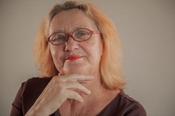 Cheerful elderly woman with red hair in glasses smiles and flirts in front of camera