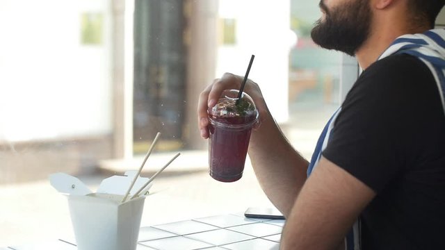 Young man drinking juice smoothie in in a cafe, urban city background