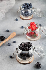 Fototapeta na wymiar strawberries, blueberries, blackberries , berries in separate glass jars on the gray background, 