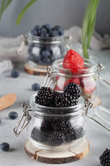 strawberries, blueberries, blackberries , berries in separate glass jars on the gray background, 