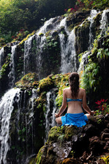 Young Caucasian woman meditating, practicing yoga at waterfall. View from back. Banyu Wana Amertha waterfall Wanagiri, Bali, Indonesia. 
