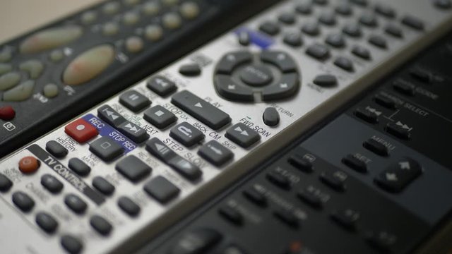 Black and silver different TV remote controls with buttons are on table