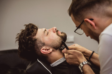 Young man with trendy haircut at barber shop. Barber does the hairstyle and beard trim.