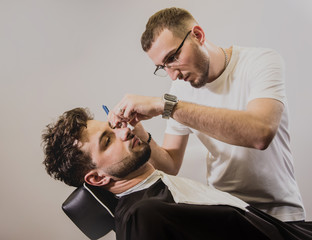Young man with trendy haircut at barber shop. Barber does the hairstyle and beard trim.