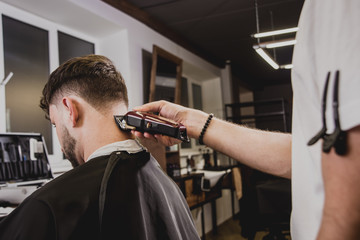 Young man with trendy haircut at barber shop. Barber does the hairstyle and beard trim.