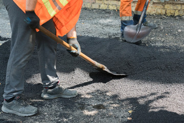 Worker man lays asphalt road repair road paving yellow sun ray light. A man in overalls is laying...