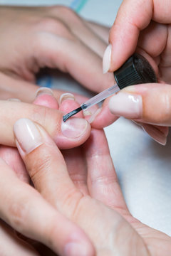 woman hand on manicure treatment with cuticle knife in beauty salon. applying a brush on acrylic nails in the salon. vertical photo