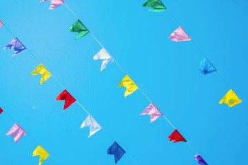 Colored flags flutter in the wind on a blue sky background. Holiday decoration. Close up.