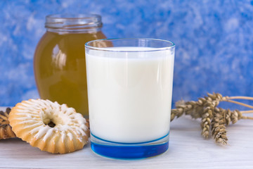 Glass of milk with cookies and honey on the table. On a light blue background.