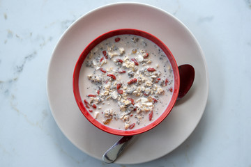 Fresh breakfast of granola, yogurt, nuts, goji berries, chia seeds and banana. Muesli with fruits and berries in red bowl