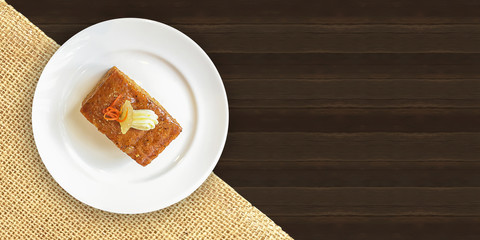 Carrot cake on white plate with sackcloth and dark wooden texture table top background.Isolated carrot cake on white plate with clipping path.