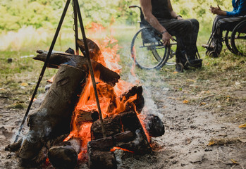 Disabled man resting in a campsite with friends. Wheelchair in the forest on the background of...