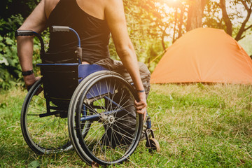 Fototapeta na wymiar Disabled man resting in a campsite with friends. Wheelchair in the forest on the background of tents