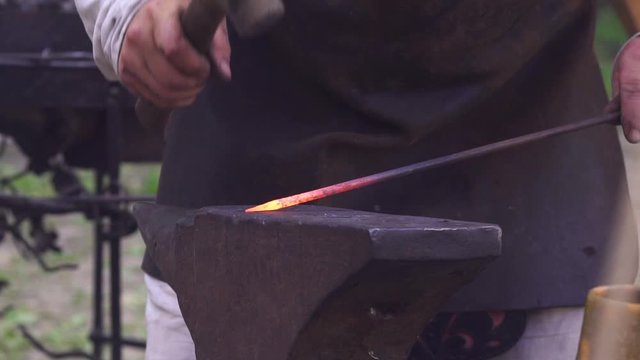 Blacksmith manually forging metal rod in outdoor smithy during Slavic and old culture days in Sobotka, Poland. Slow motion.