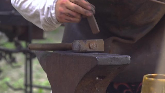 Blacksmith presents possible use of traditional cut-off hardy tool and then takes it off his anvil. Slavic and old culture days in Sobotka, Poland. Slow motion.
