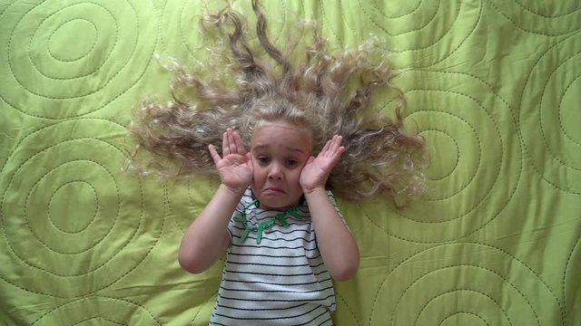 Little blond girl lying on bed and play hide seek. Gimbal motion top view