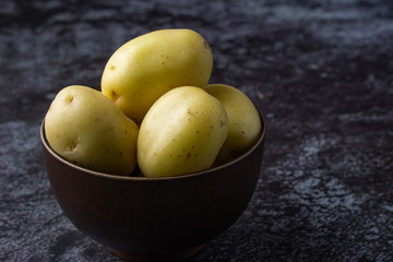 Raw potatoes in a bowl on dark background. Selective focus.