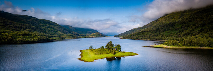 aerial view of loch leven near kinlochleven and glen coe in the argyll region of the highlands of scotland with a green island in the foreground and calm blue waters with misty mountains - obrazy, fototapety, plakaty