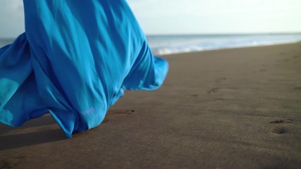Legs of a woman in beautiful blue dress walking along a black volcanic beach