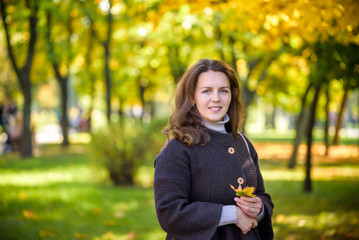 Young woman with autumn leaves in hand and fall yellow maple garden background