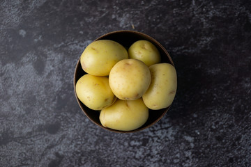 Raw potatoes in a bowl on dark background. Selective focus.