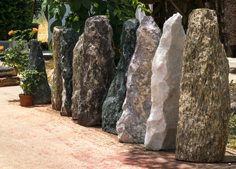 Large tall stones of different colors standing in a row in the yard. Stone fence or wall