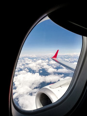 Fototapeta premium View outside the porthole of a wing of a modern airplane flying over the clouds with blue sky. View from the aircraft window during a tourist flight. Travel, tourism, transport and freedom concept.