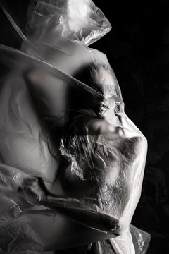 Slim girl dressed only in underwear emotionally posing, wrapped in fluttering in the wind and fitting her graceful young body cellophane film. Artistic, creative, abstract design. Black and white